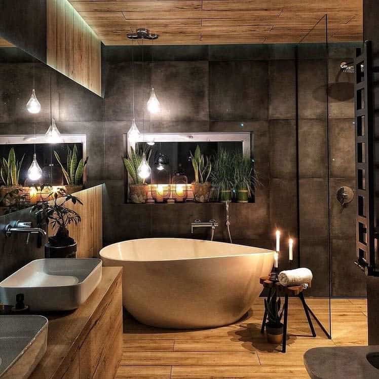 Stylish wet room with a freestanding bathtub, plants, pendant lights, wood and dark tiles, candles, and a large mirror