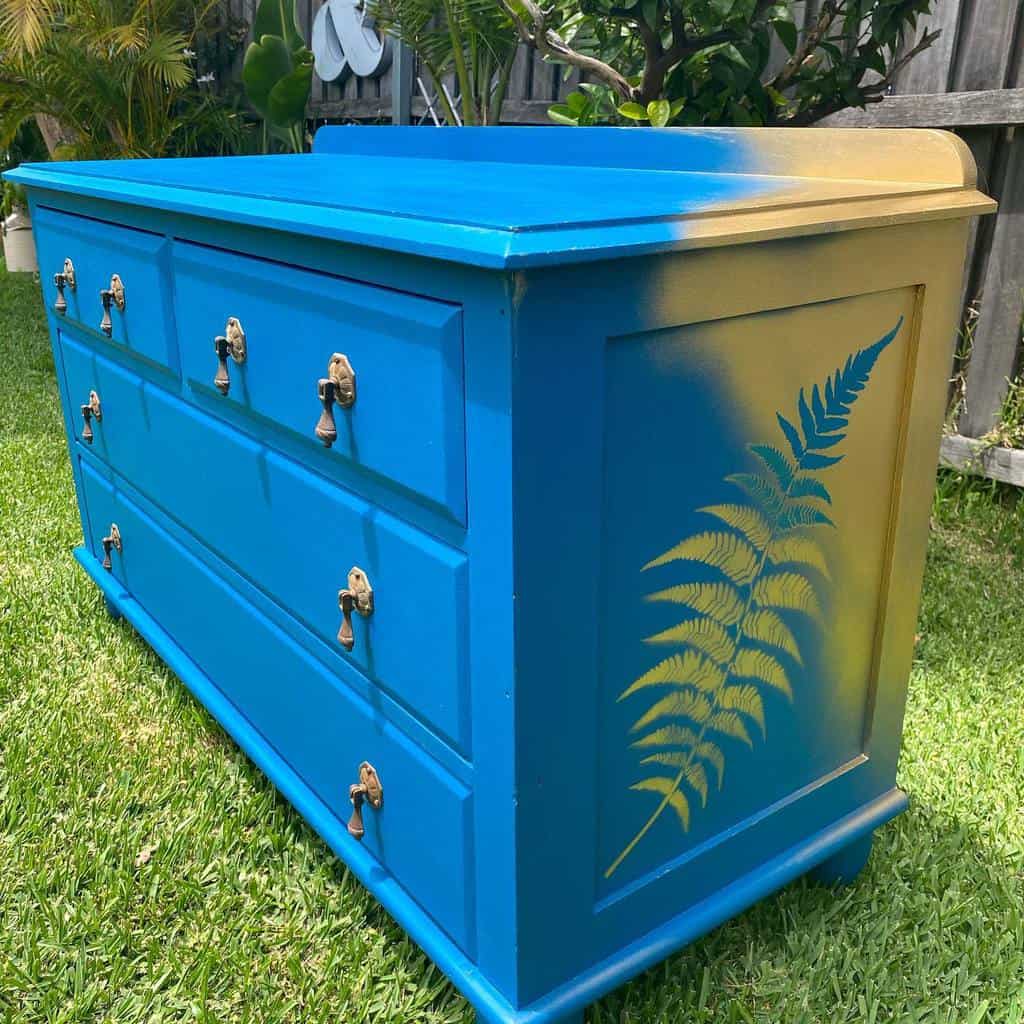 Bold blue and gold chalk-painted dresser with a fern stencil design, featuring antique brass handles for a striking two-tone effect