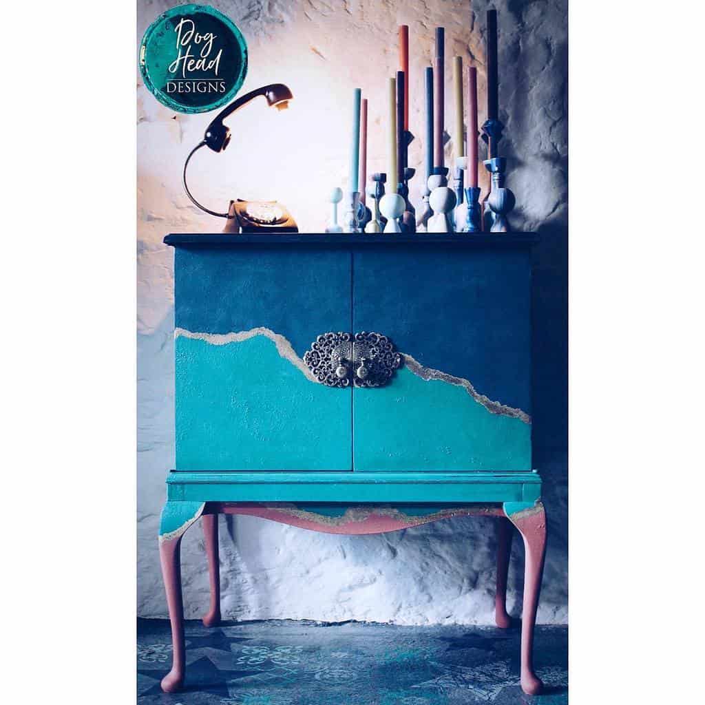 Artistic chalk-painted cabinet with deep blue, teal, and pink tones, accented by gold detailing and ornate metal hardware for a bold look