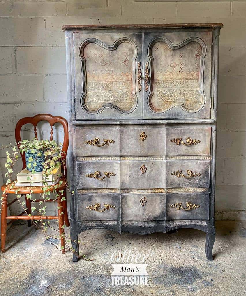 Antique armoire with distressed chalk paint finish, ornate gold handles, and faded stencil detailing for a vintage European-inspired look