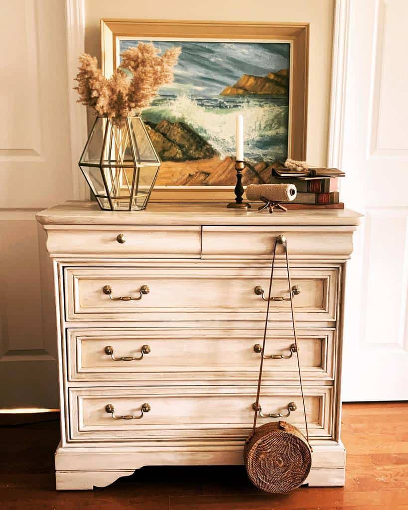 Vintage-style dresser with a distressed white chalk paint finish, antique brass handles, and warm coastal-inspired decor for a timeless look