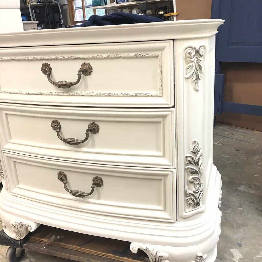 Elegant vintage dresser with ornate detailing, painted in soft white chalk paint, featuring antique brass handles for a classic French-inspired look