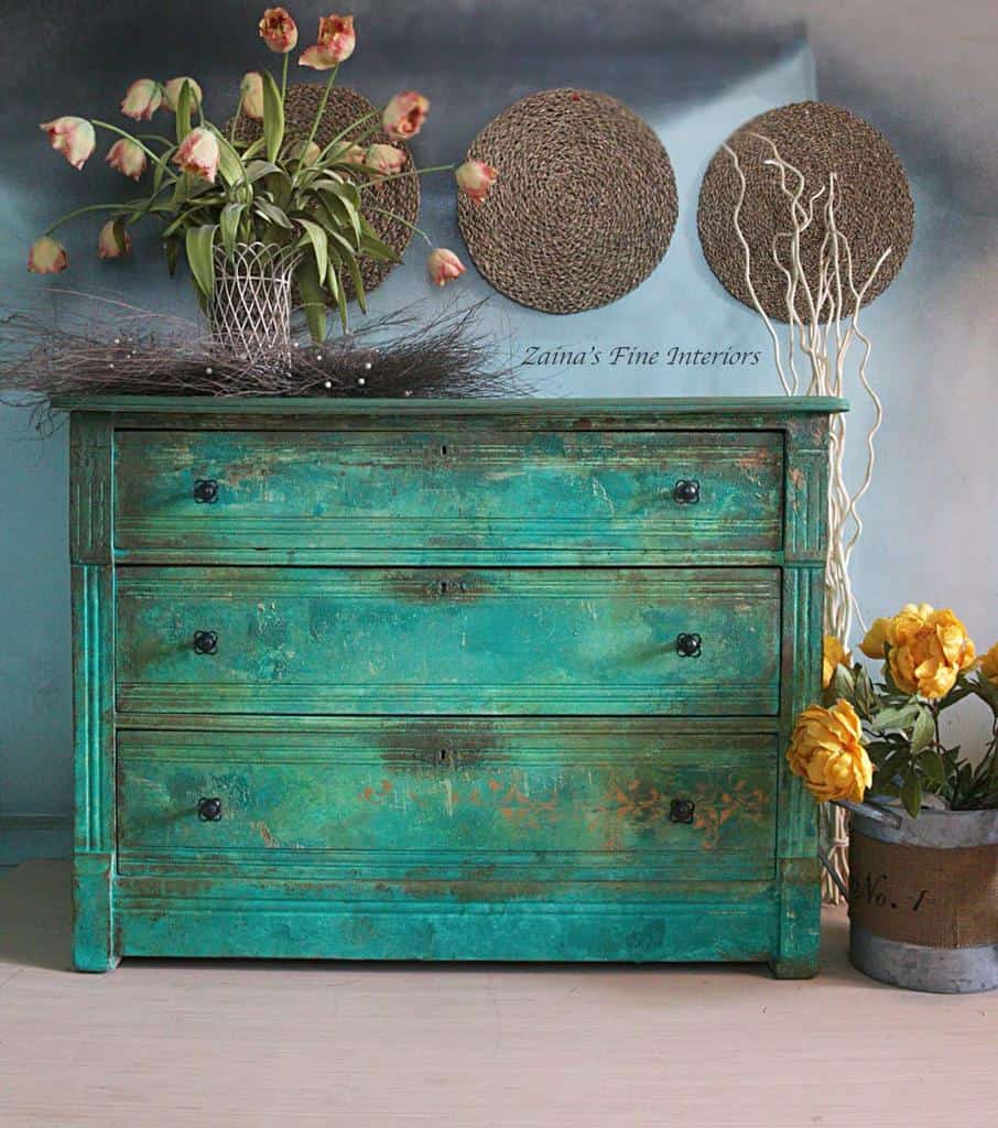 Rustic turquoise dresser with a distressed chalk paint finish, aged patina, and black knobs, adding vintage charm to the space