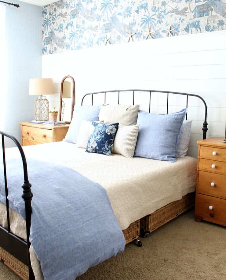 Bedroom with black metal bedframe, blue and white bedding, wooden bedside tables, and tropical wallpaper accent on upper wall