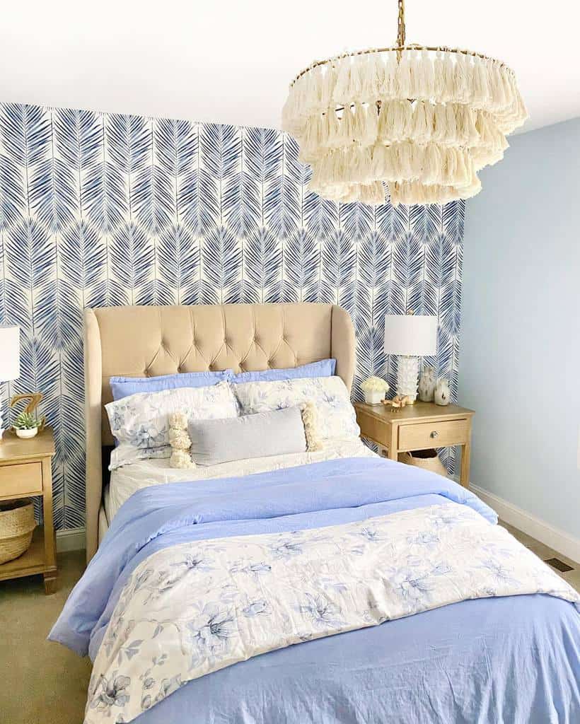 Bedroom with a tufted headboard, blue and floral bedding, wooden nightstands, and a fringe chandelier against a leaf-patterned wall