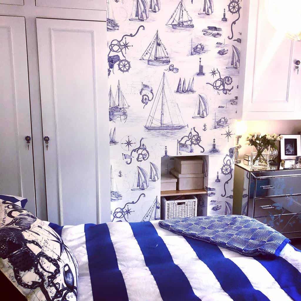 Nautical-themed bedroom with a sailboat-patterned wall, blue striped bed, mirrored dresser, and a small shelf with decorative items