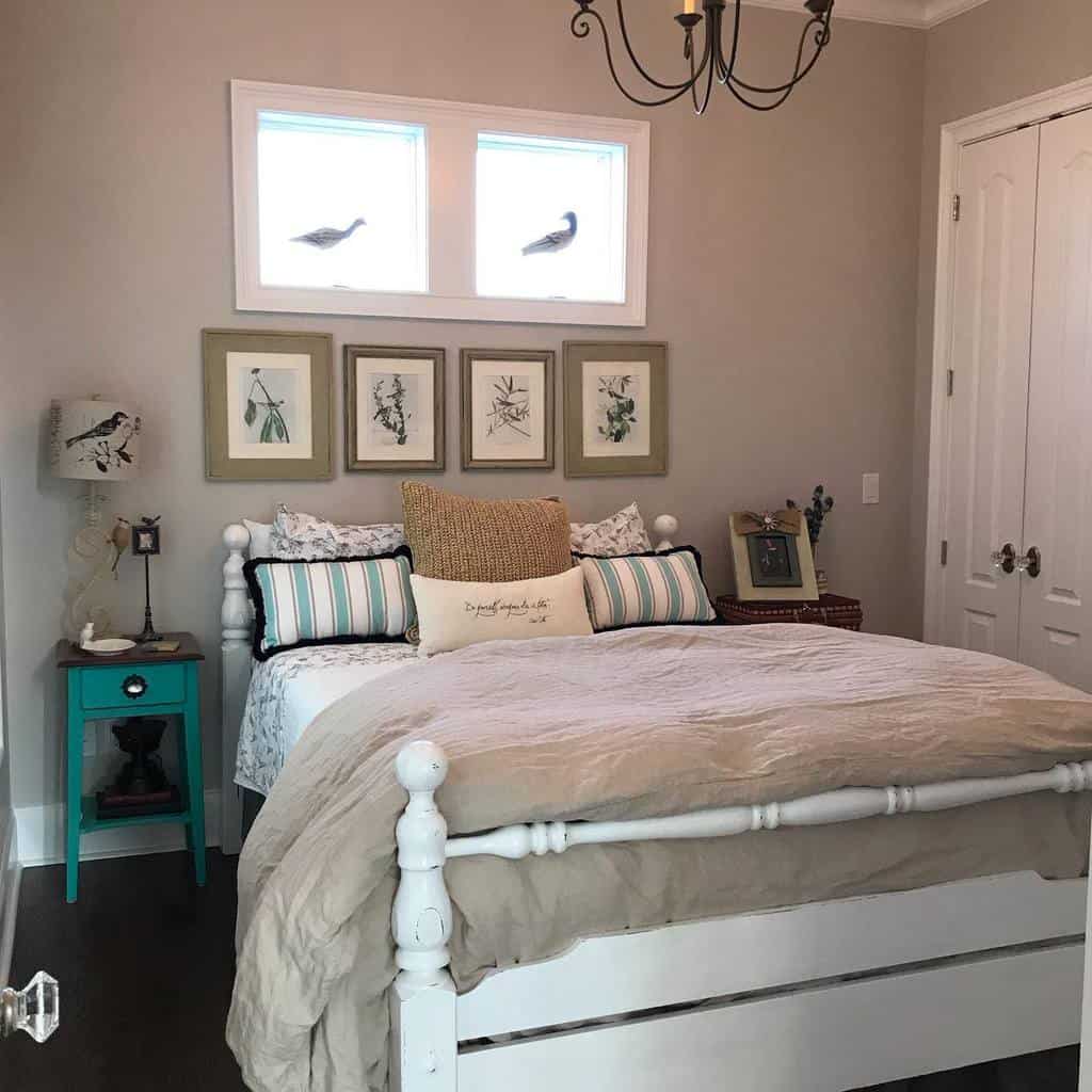 Cozy bedroom with a white bed, decorative pillows, teal nightstand, bird-themed art, and a chandelier under three small windows