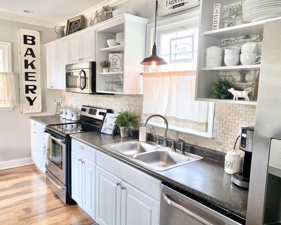 White open shelves display neatly stacked dishes, mugs, and greenery, adding charm to a bright farmhouse-style kitchen with vintage decor