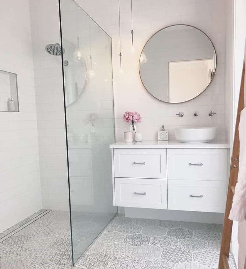 Modern wet room with glass shower, round mirror, white vanity, vessel sink, pink flowers, and geometric patterned floor tiles