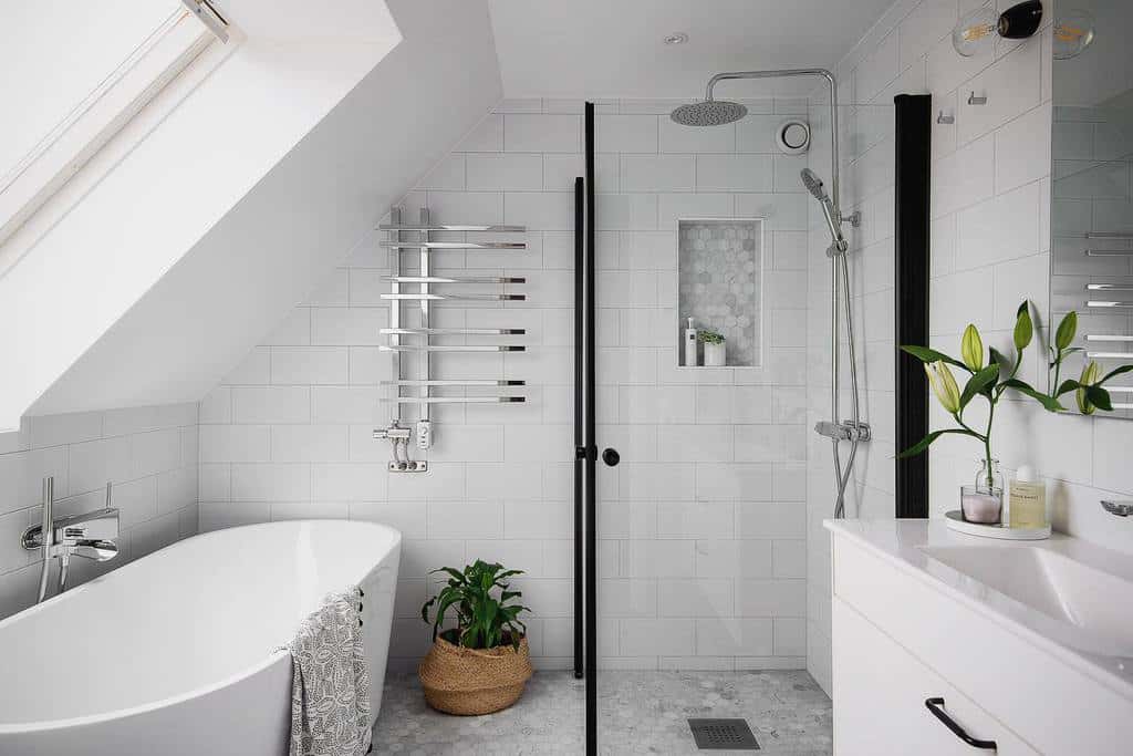 Scandinavian-style wet room with a freestanding tub, black-framed shower, white subway tiles, and natural accents for a fresh, modern look