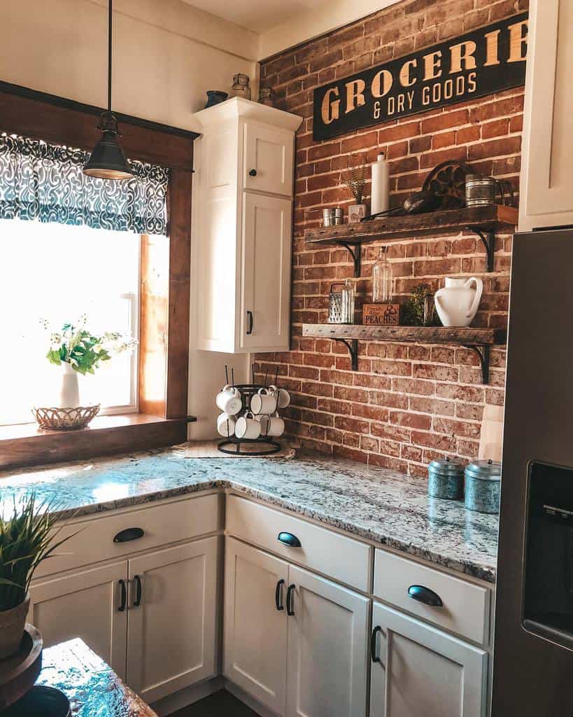 Rustic wooden shelves with black metal brackets hold jars, mugs, and vintage decor, enhancing the farmhouse charm of a brick-walled kitchen