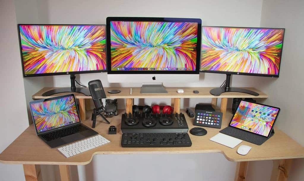 Home office with an iMac, two monitors, a laptop, a tablet, and various accessories on a wooden desk