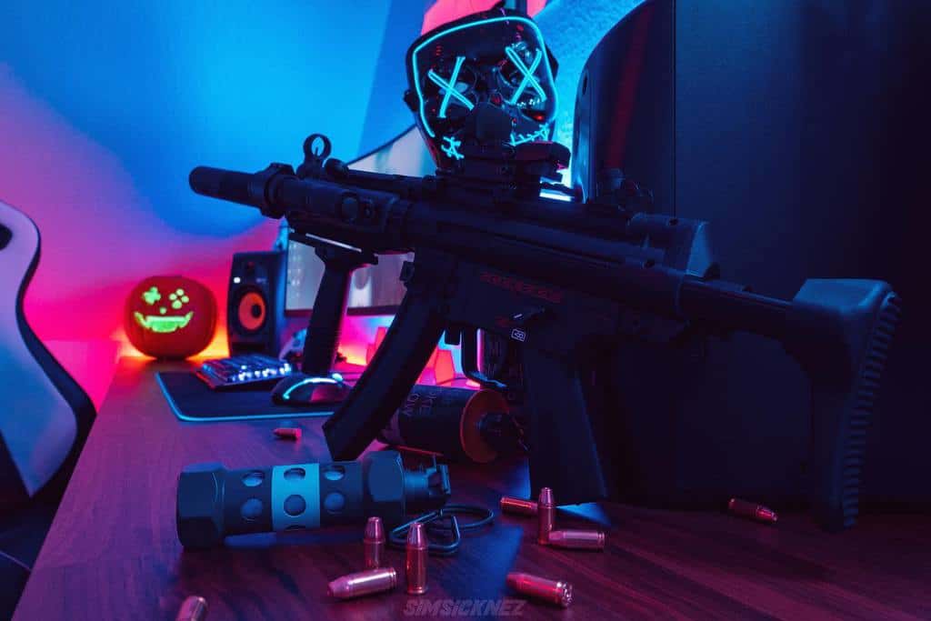 Neon-lit gaming setup with a rifle, ammo, and a pumpkin with a smiling face mask on the desk