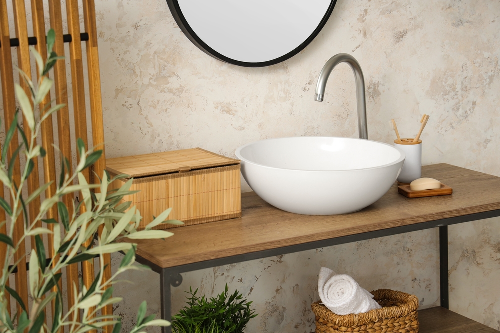 Minimalist bathroom with a round mirror, white sink, and wooden decor elements.