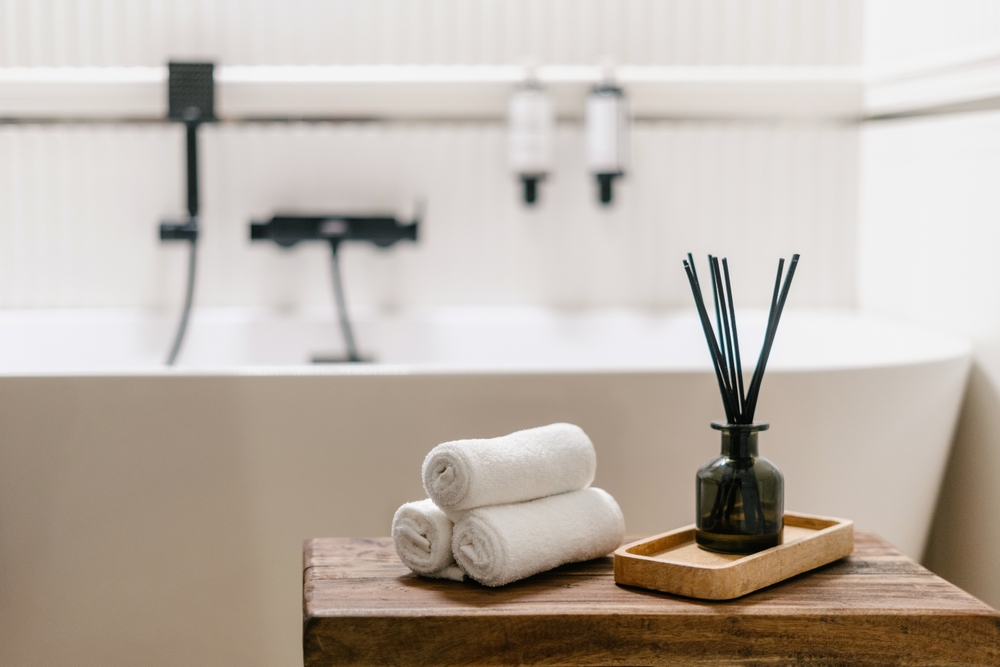 A bathtub with rolled towels and a reed diffuser on a wooden surface nearby.