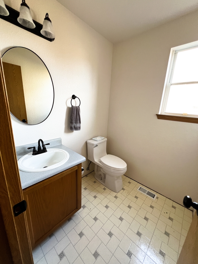 A clean bathroom with a toilet, sink, mirror, towel, window, and light fixture