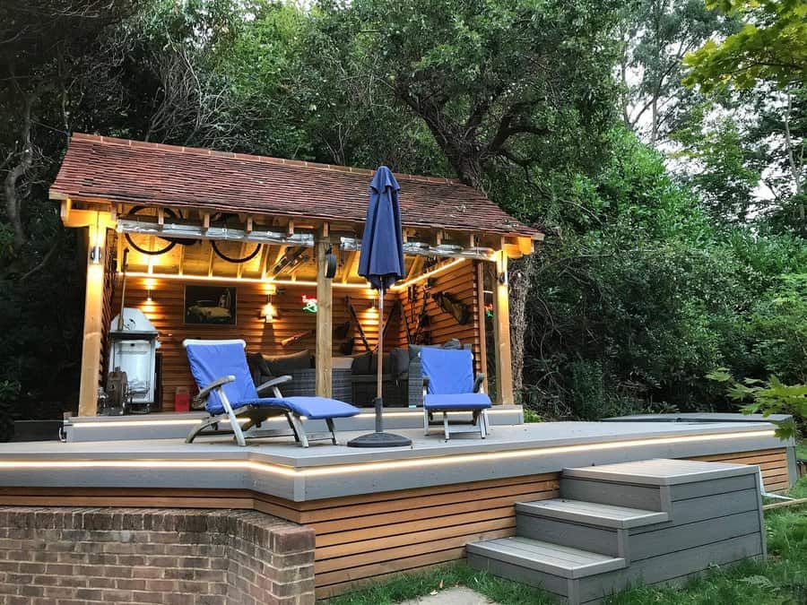 Outdoor bar on deck with lighting and loungers in a wooded area