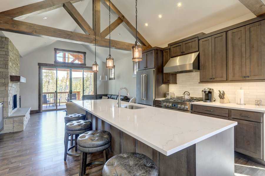 Modern kitchen with vaulted ceiling, wooden beams, stainless steel appliances, large island with bar stools, and rustic lighting fixtures
