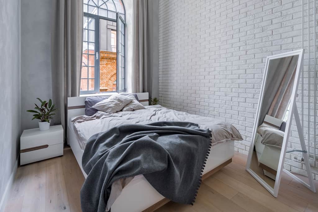 bedroom with white brick wall and a mirror facing in a bed