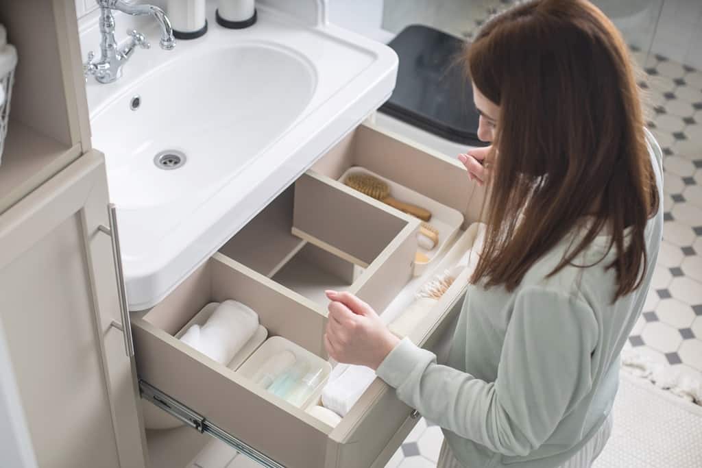 woman organizing an open drawer in a bathroom with sink