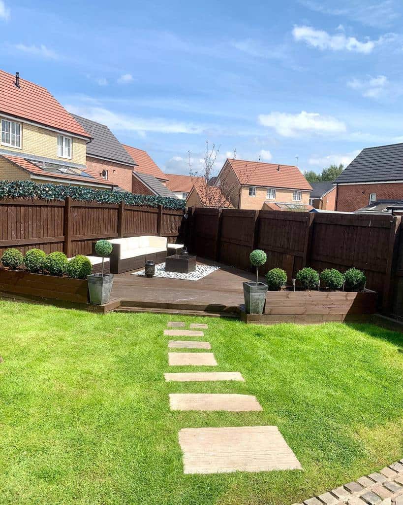 Backyard with a wooden privacy fence, raised deck seating, and neatly trimmed shrubs, creating a cozy and secluded outdoor relaxation space