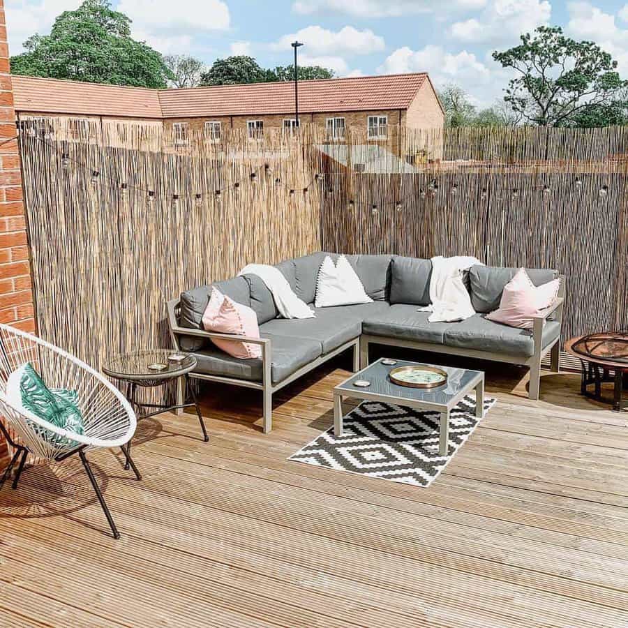 Cozy outdoor deck with a bamboo privacy screen, grey sectional sofa, pastel cushions, and a modern coffee table, creating a stylish and relaxed retreat