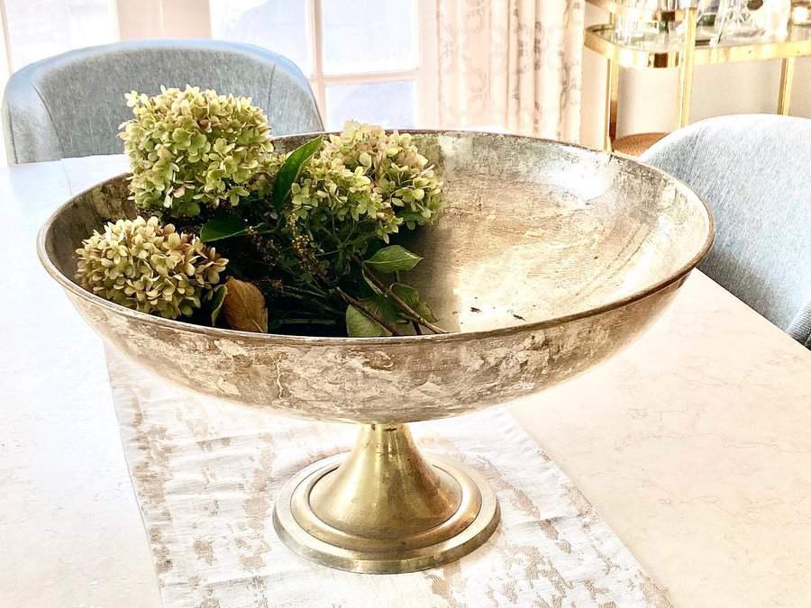 A large metallic bowl on a dining table centerpiece with green hydrangeas inside