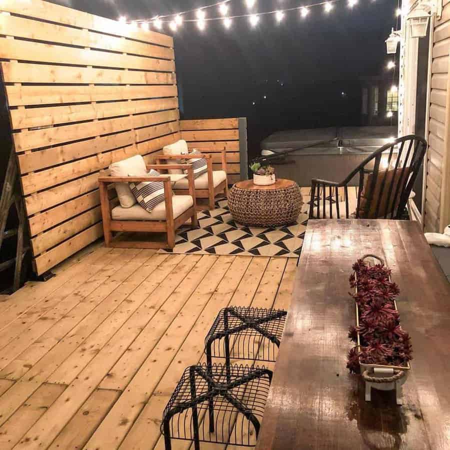 Cozy outdoor deck with a DIY wooden privacy screen, cushioned chairs, string lights, and a rustic dining table, creating a warm and inviting atmosphere