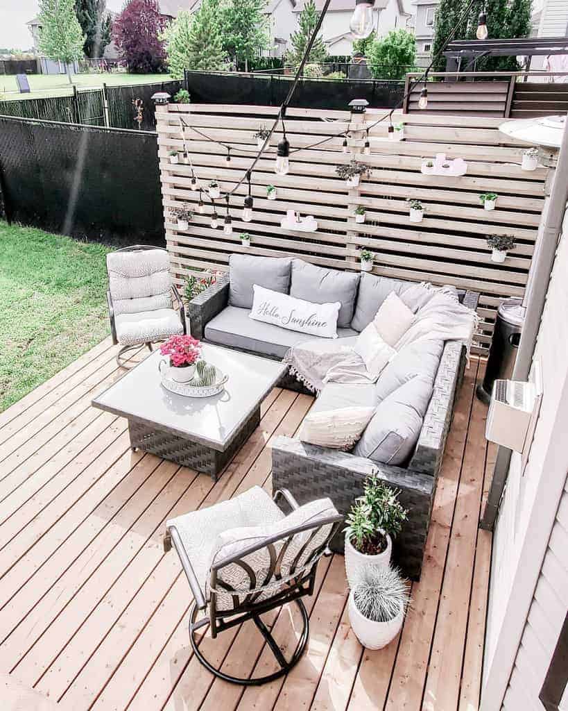 Modern backyard deck with a DIY wooden slat privacy screen, cozy grey sectional sofa, hanging planters, and string lights for a stylish outdoor retreat