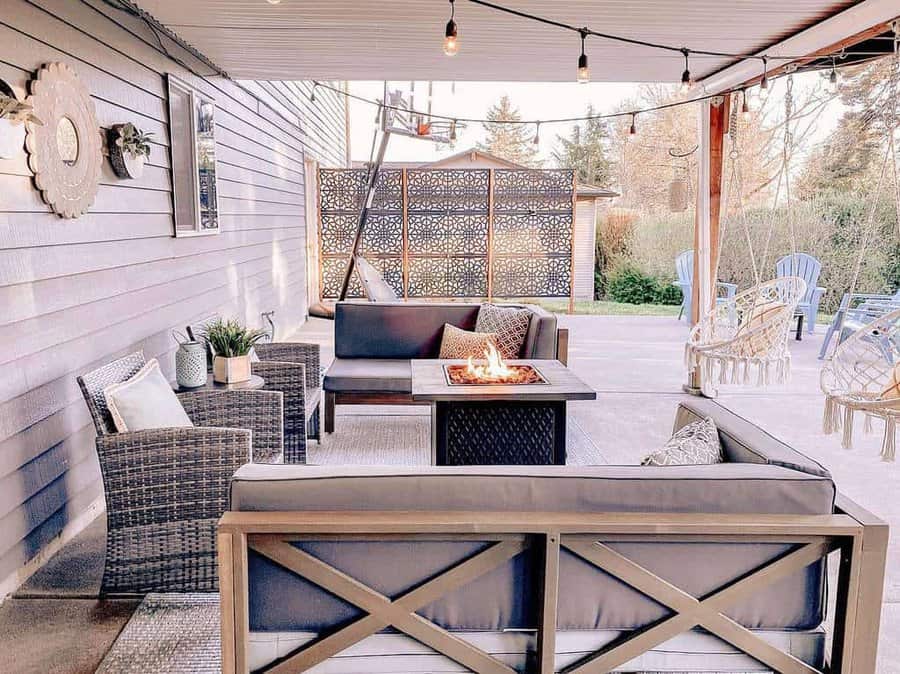 Stylish covered patio with a decorative privacy screen, cozy seating, fire pit table, string lights, and hanging chairs for a warm and inviting outdoor retreat