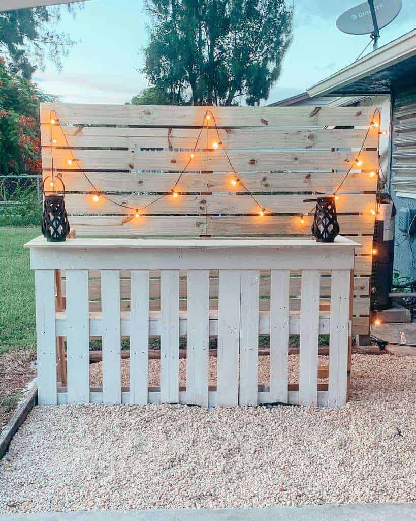 DIY outdoor privacy screen made of wooden slats, decorated with string lights and lanterns, creating a charming and cozy backyard ambiance