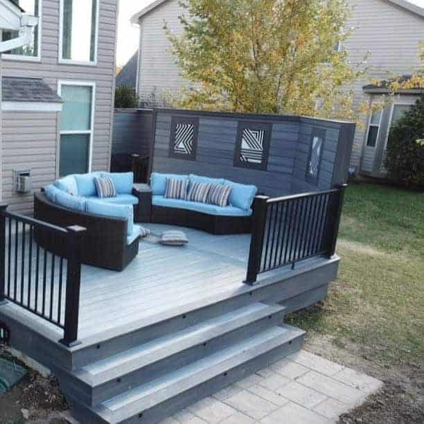 Elevated backyard deck with a modern privacy screen, black railing, and cozy blue cushioned seating, creating a stylish and private outdoor lounge area