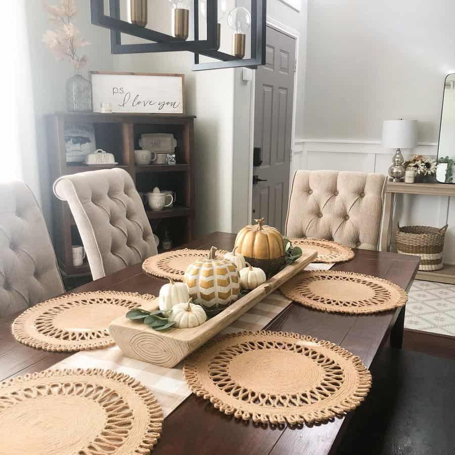 Fall-themed dining table decor with a wooden tray centerpiece holding decorative pumpkins and greenery, paired with woven placemats