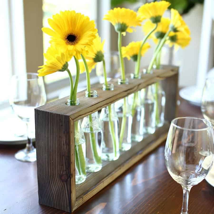 Yellow flowers in a wooden-framed glass vase centerpiece on a table