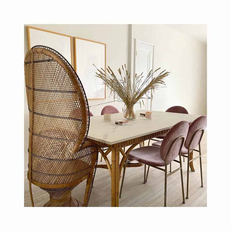 Minimalist dining space with a rattan chair, soft pink velvet chairs, and a simple dried grass centerpiece in a glass vase