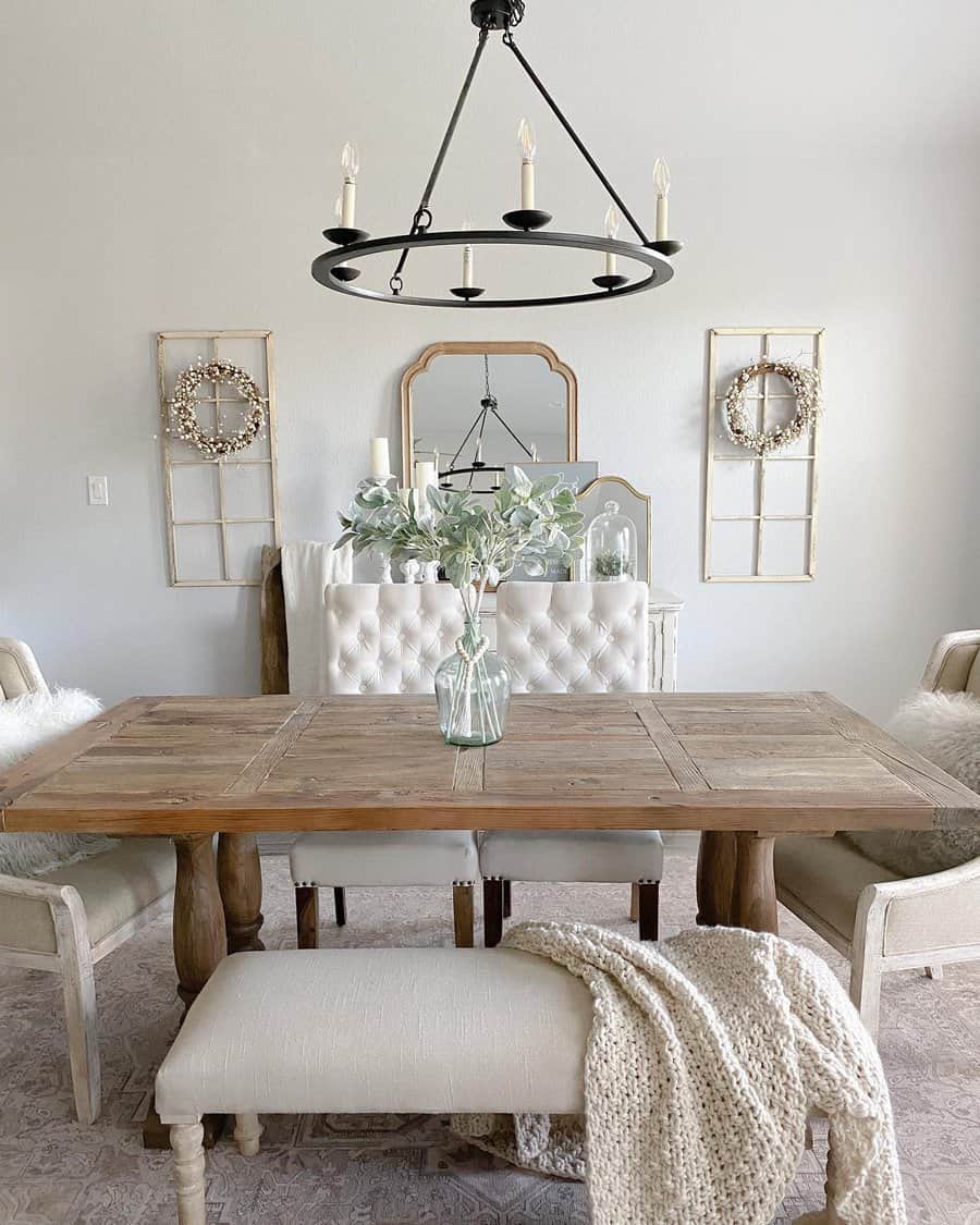 Rustic farmhouse dining room with a wooden table, a simple glass vase with greenery, tufted seating, and cozy neutral decor