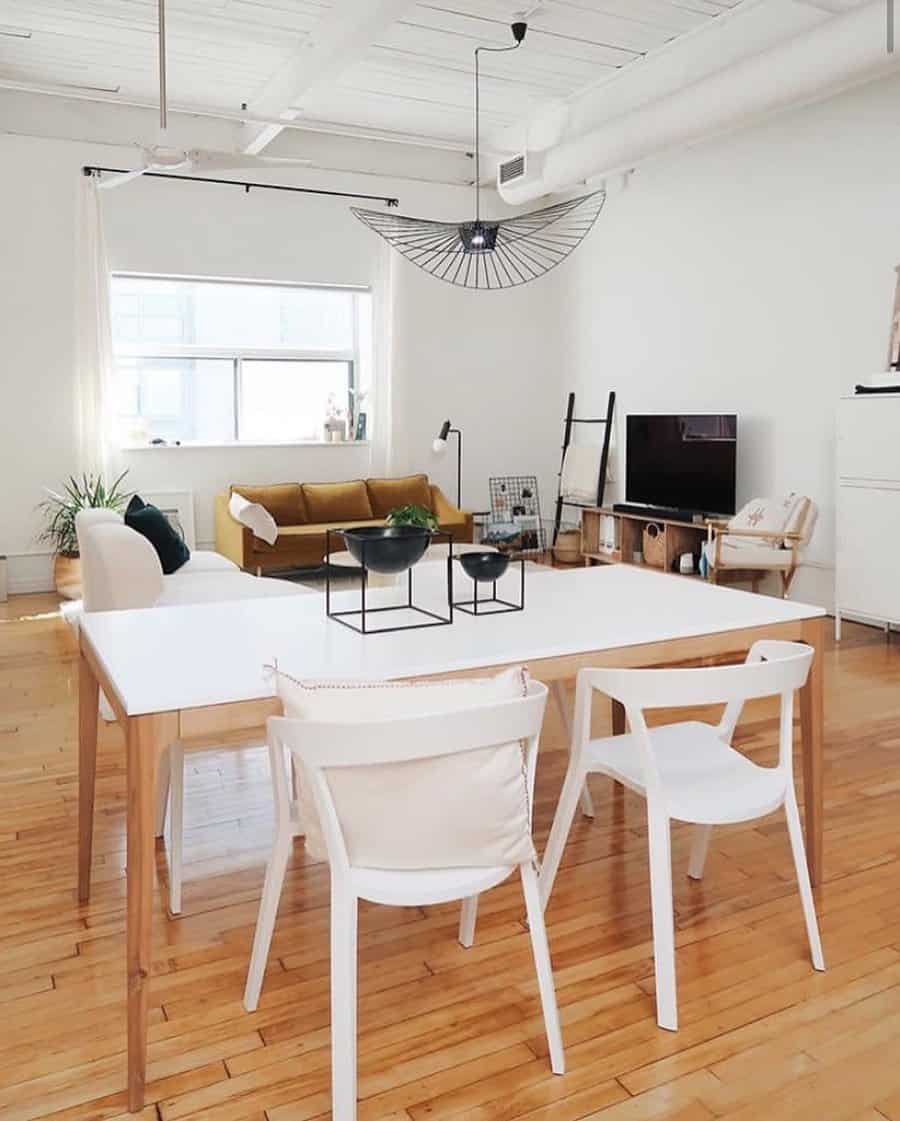 Minimalist dining area with a sleek white table, modern black metal bowl centerpiece, white chairs, and an open-concept living space