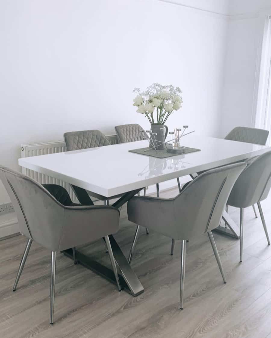 Modern dining room with a white table and six gray chairs, decorated with a vase of white flowers on a wooden floor