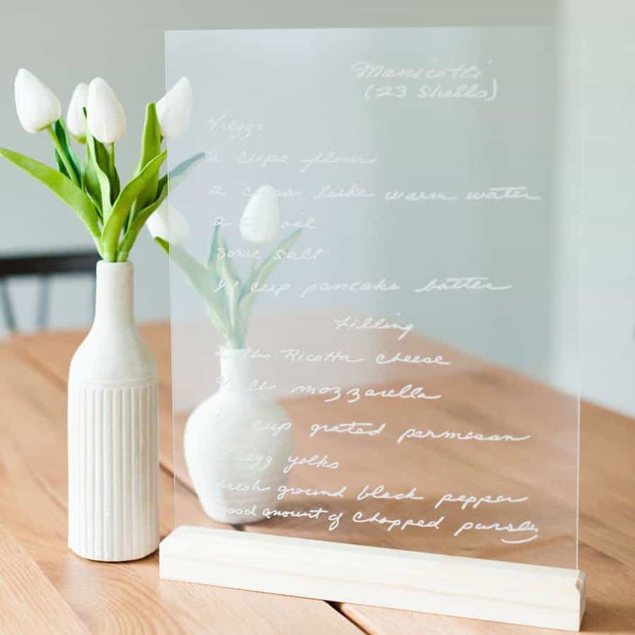 Clear recipe card on a wooden stand beside a vase with white tulips on a wooden table