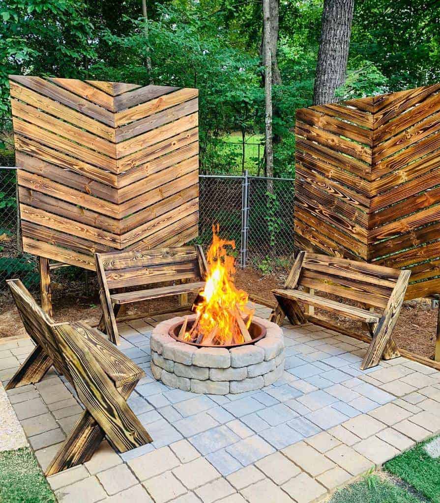 Backyard fire pit area with a rustic wood privacy screen, matching wooden benches, and a stone fire pit, creating a cozy and inviting outdoor gathering space