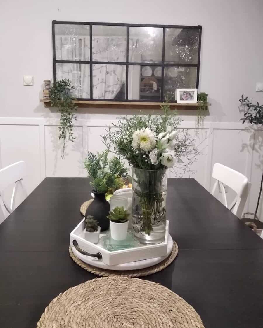 Modern dining table with a white tray centerpiece holding fresh flowers, greenery, and small potted plants, adding a natural touch