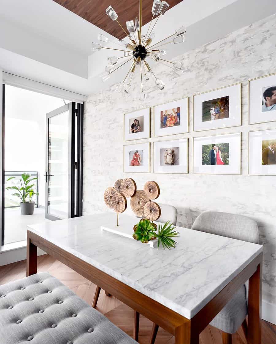 Modern dining room with a marble-top table, tufted bench, sculptural wood centerpiece, gold chandelier, and framed gallery wall