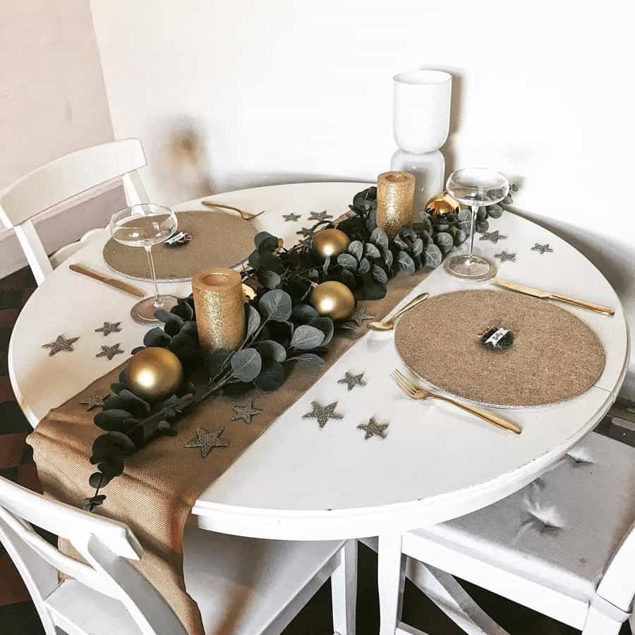 Festive table with gold candles, ornaments, eucalyptus, and star decorations on a white tablecloth set for two