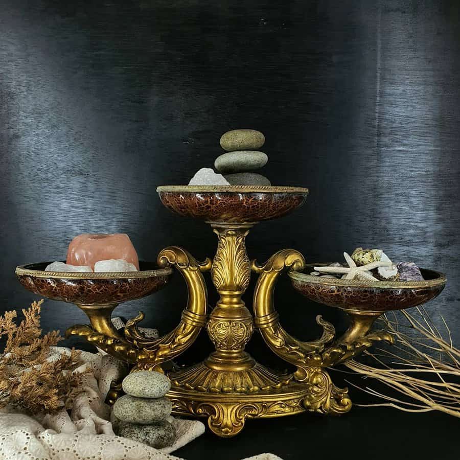 Elegant gold stand with three bowls holding stones, shells, and a starfish, decorative lace and dried plants surround the setup