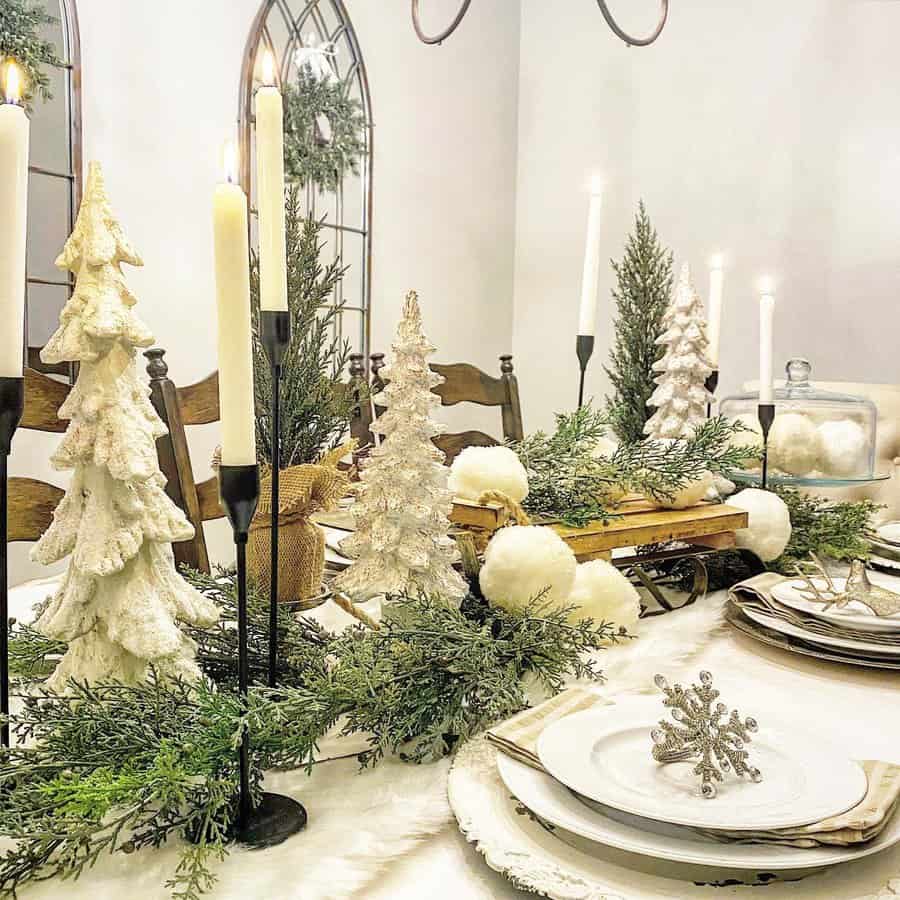 Festive dining table with snow-covered tree decorations, tall candles, greenery, and snowflake napkin rings; cozy holiday setting