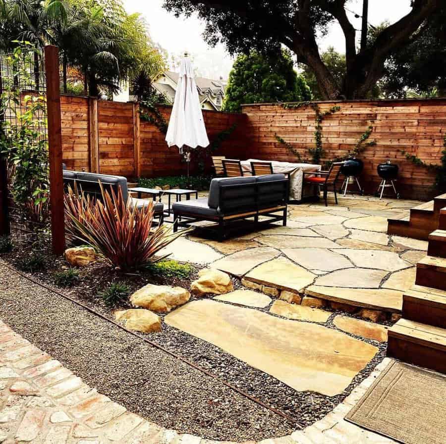 Cozy backyard patio with a wooden privacy fence, stone pavers, modern outdoor seating, a dining area, and lush greenery for a stylish and inviting space