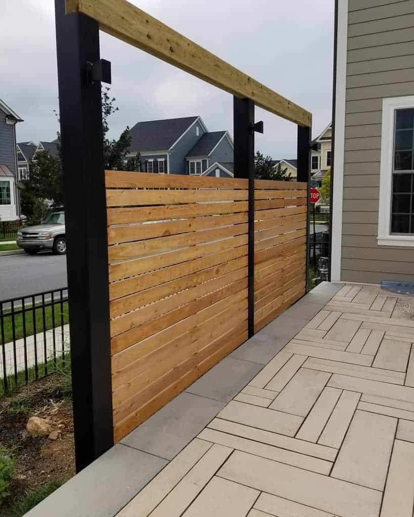 Modern outdoor privacy screen with horizontal wooden slats framed by black metal posts, creating a sleek and stylish barrier for a contemporary patio space