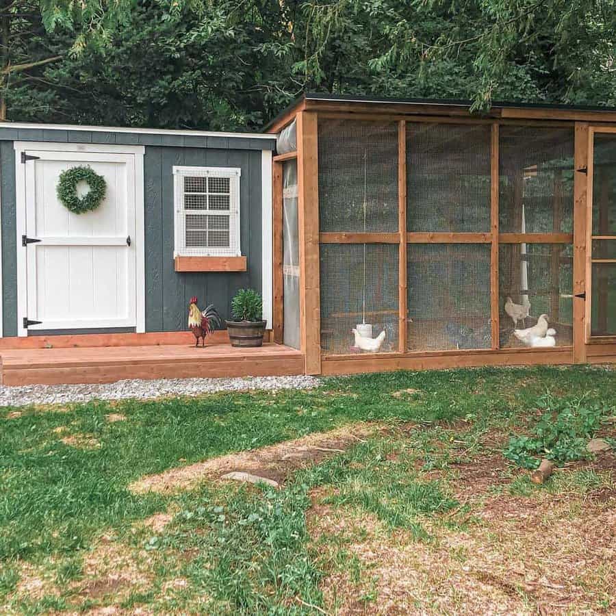 Cozy chicken coop with a dark wall, white door, and wreath; chickens inside a mesh enclosure; greenery in the background