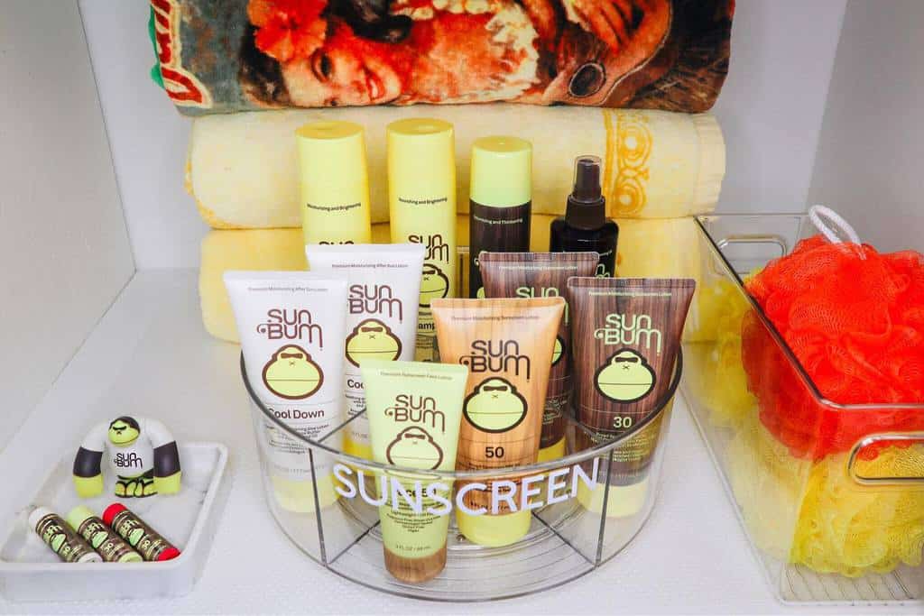 Organized bathroom shelf with a turntable tray holding Sun Bum sunscreen, towels, and bath accessories for a neat and functional space