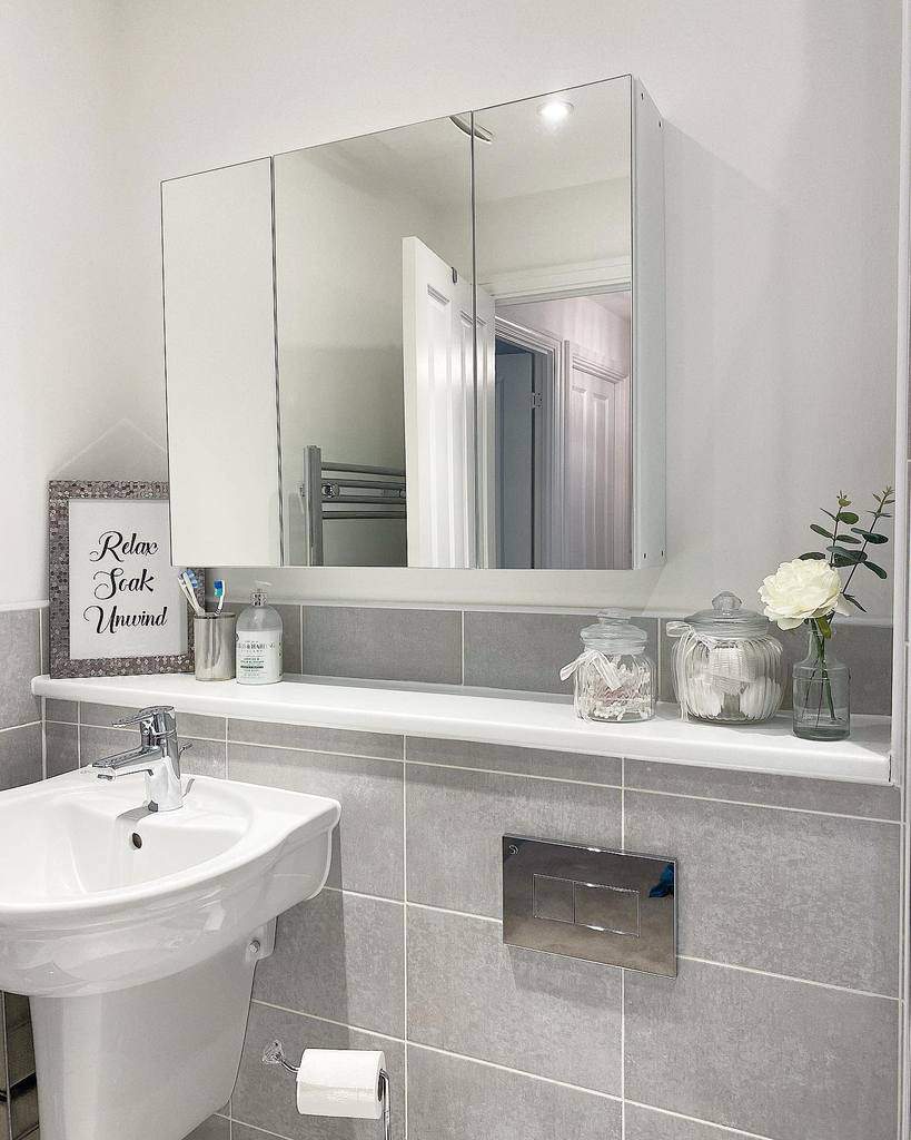 Minimalist bathroom with a mirrored cabinet, built-in shelf, and glass jars for organized storage in a sleek, modern space